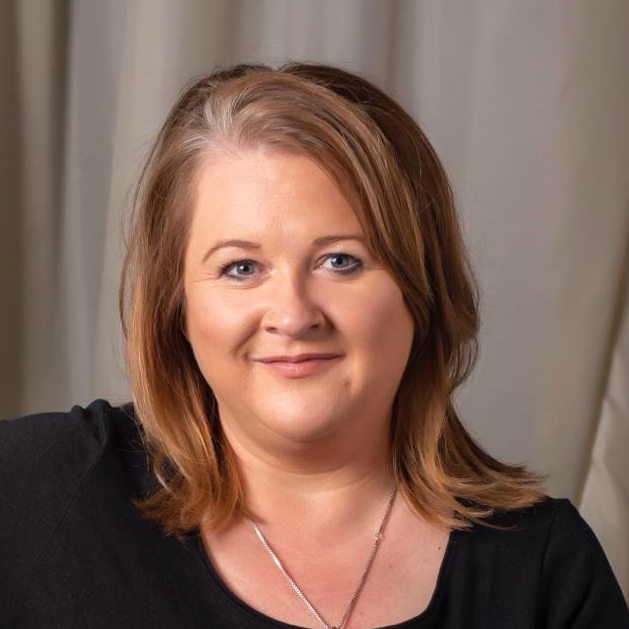 Cath Byford, NSFT’s Chief People Officer and Deputy Chief Executive Officer, pictured smiling. She is wearing a black top in front of a grey background..